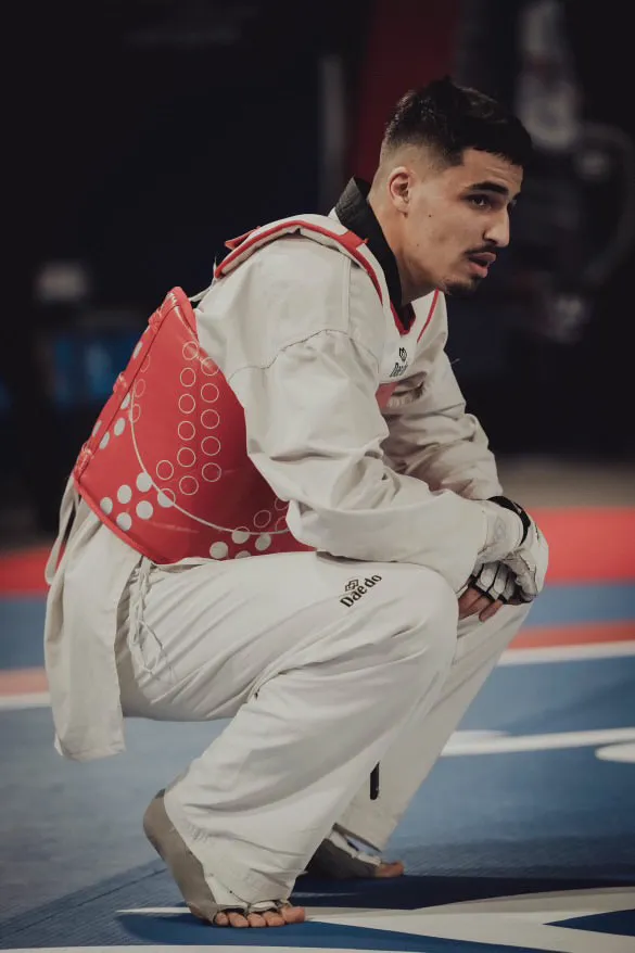 Nahil Mehnana, en dobok et plastron rouge, accroupi au bord de l'aire de combat